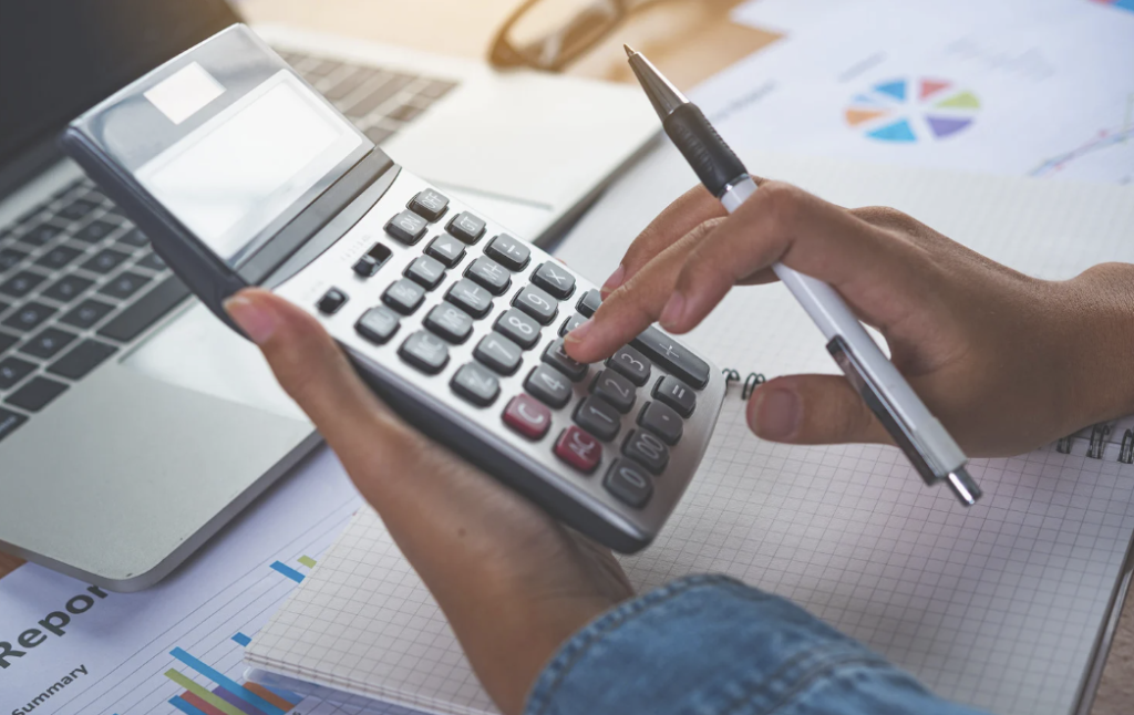 a person using a calculator on a desk in front of a laptop